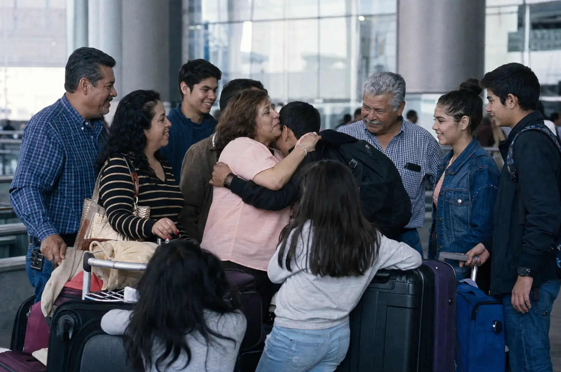 Una familia numerosa se reencuentra y se abraza en la sala de llegadas de un aeropuerto, con maletas alrededor